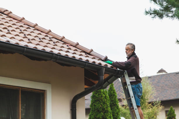 A man stands on a metal staircase and repairs a tiled roof against a cloudy sky for Affordable Roofing of Atlanta.