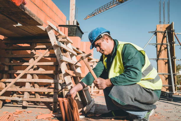A man wearing a hard hat and safety vest is diligently working on a brick wall construction site for Affordable Roofing of Atlanta.