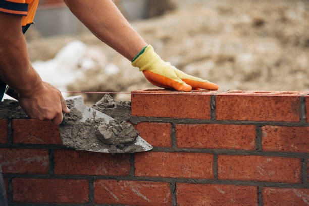 A construction worker lays a red brick with a trowel, spreading mortar, showcasing expert craftsmanship in Douglasville Georgia Masonry
