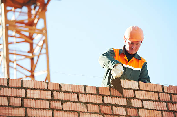 A construction mason expertly installs red bricks outdoors using a trowel and putty knife, ensuring precision in Douglasville Georgia Masonry