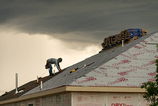  A man installing an asphalt roof on a house, using tools and materials for the roofing process.