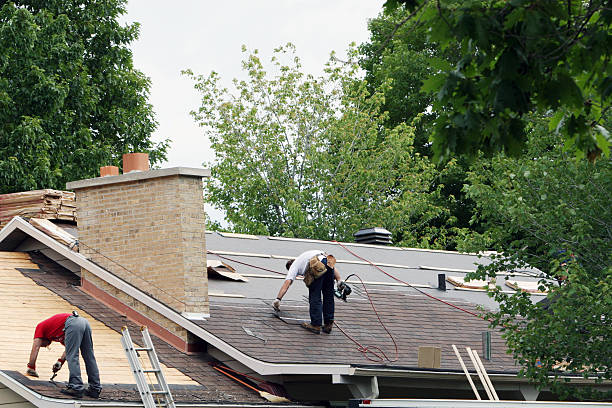 Two man working on the installation of an asphalt roof atop a house, focused on securing the roofing materials.

