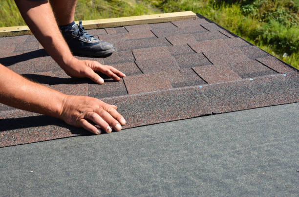 A man working on the installation of an asphalt roof atop a house, focused on securing the roofing materials.
